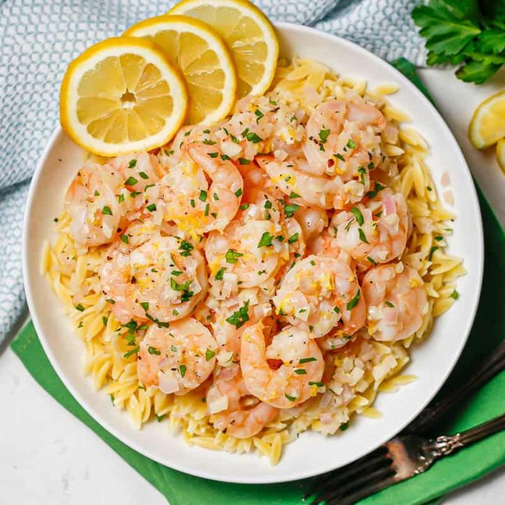 Shrimp served over top or orzo pasta with lemon slices and parsley to the side.