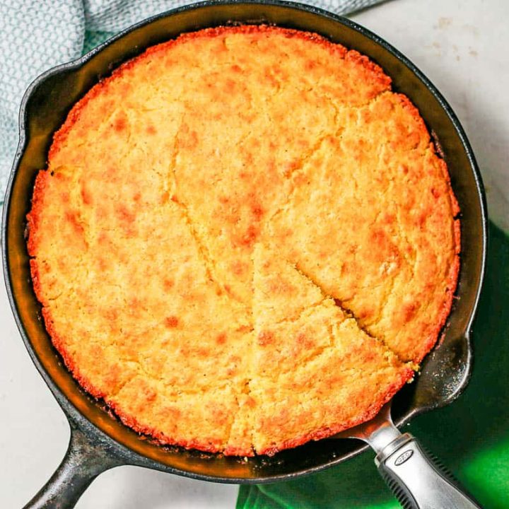 A pie server lifting up a slice of golden brown cornbread from a cast iron skillet.
