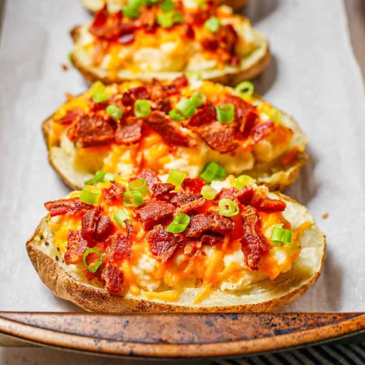 A row of twice baked potatoes on a parchment paper lined baking pan.