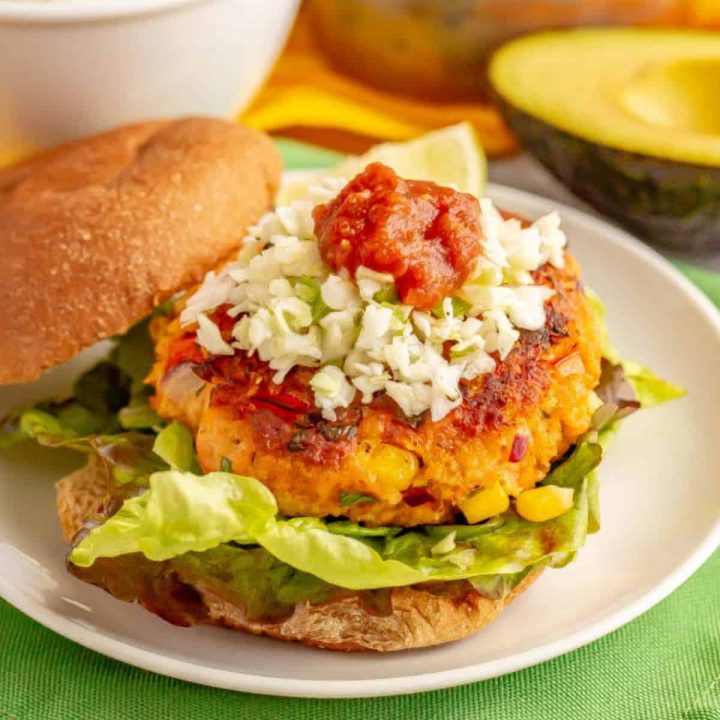 Close up of a southwestern style salmon burger served with coleslaw and salsa on top.